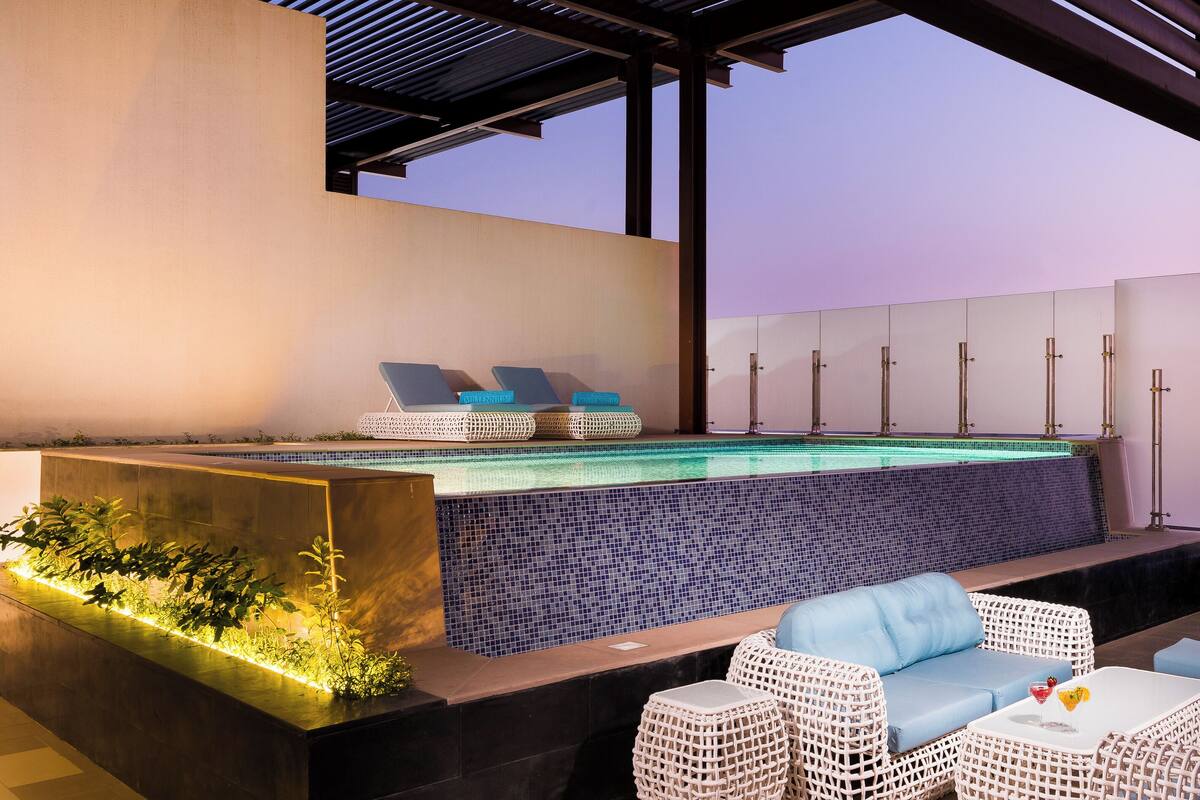 A rooftop pool area with a pergola, lounge chairs, and a small seating area.