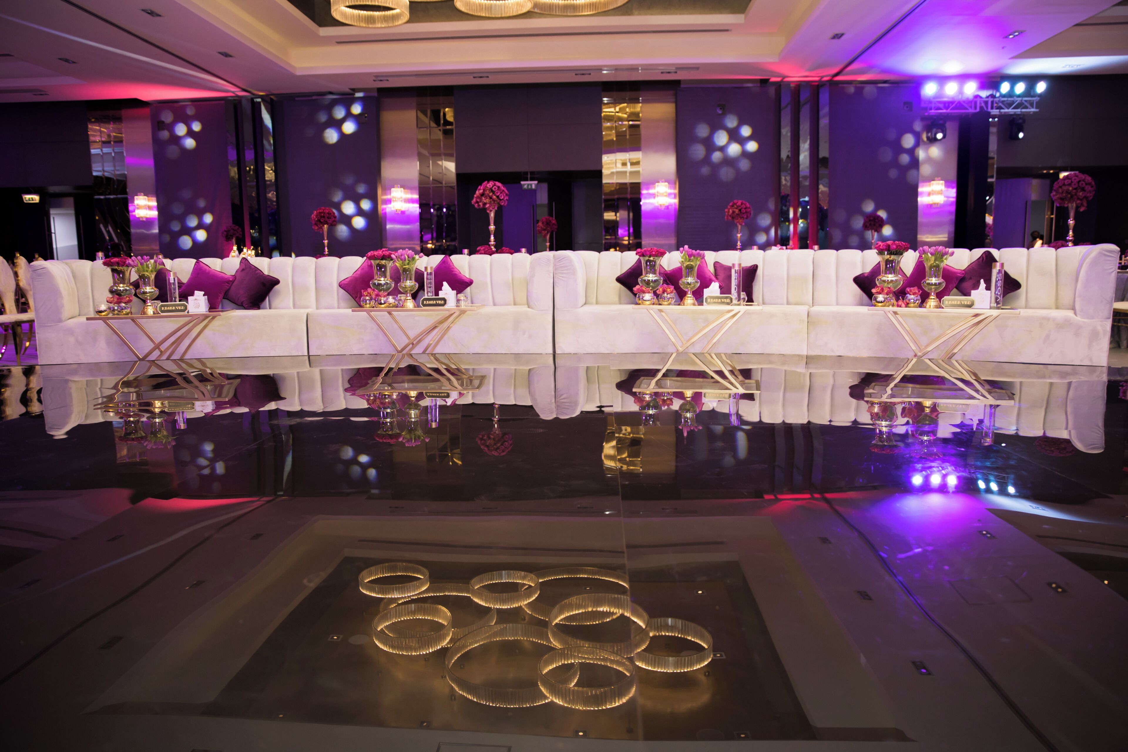 Un hall d’hôtel luxueux avec un sol réfléchissant, des canapés blancs et des touches de couleur violette.