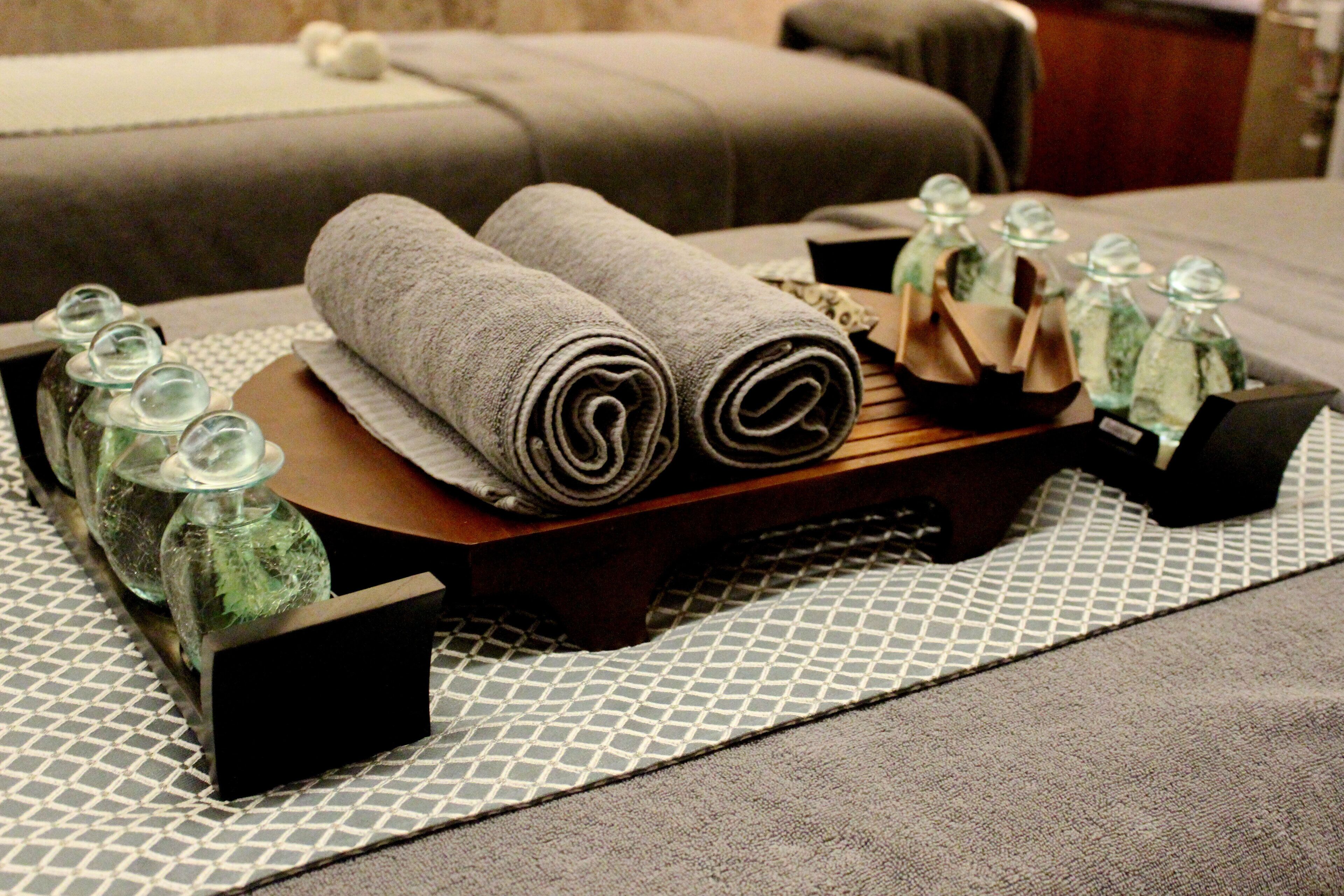 Zona de spa ordenada con toallas, botellas y una bandeja de madera sobre un tapete estampado.