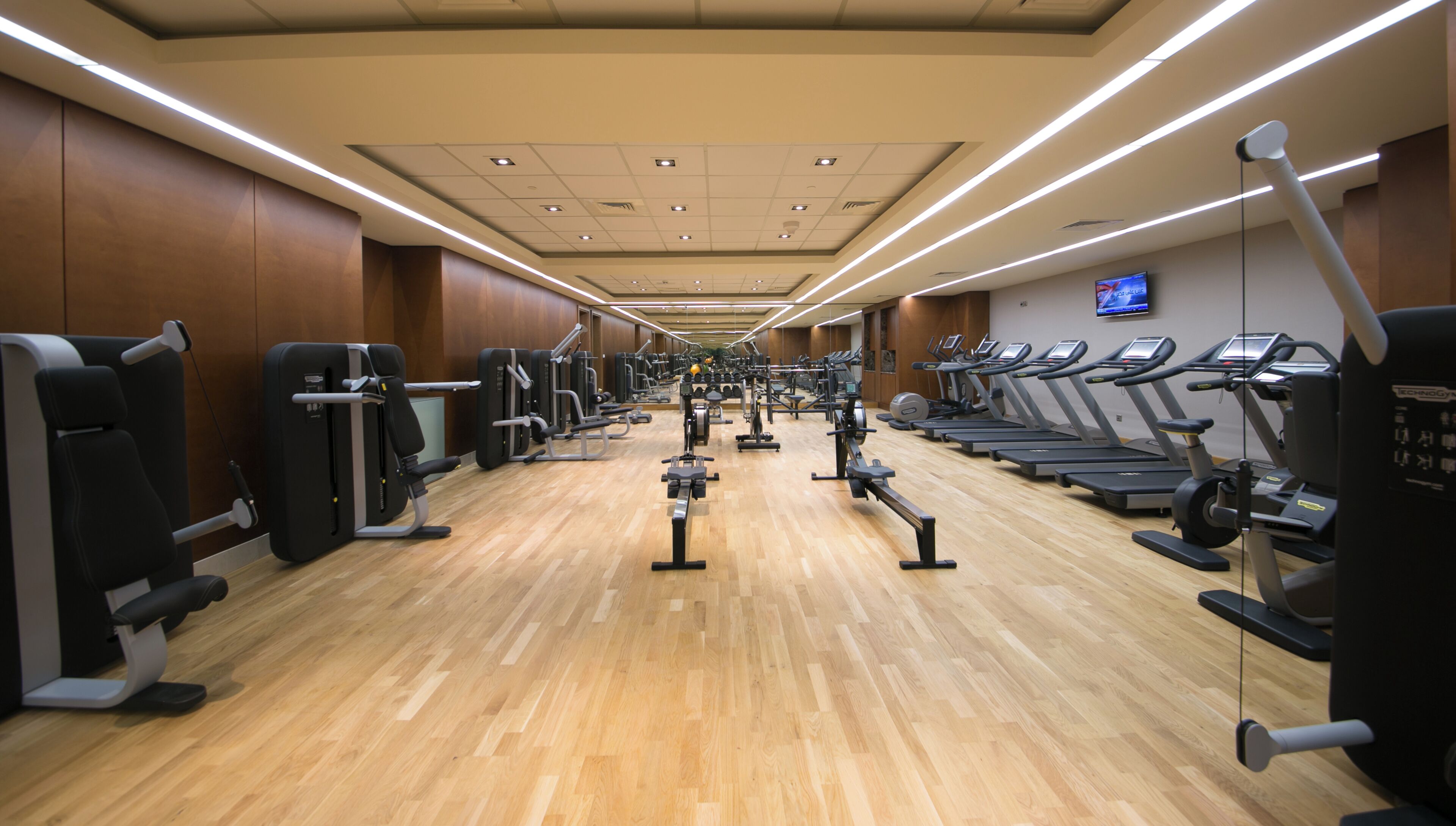 A gym with exercise equipment, wooden flooring, and a TV on the wall.