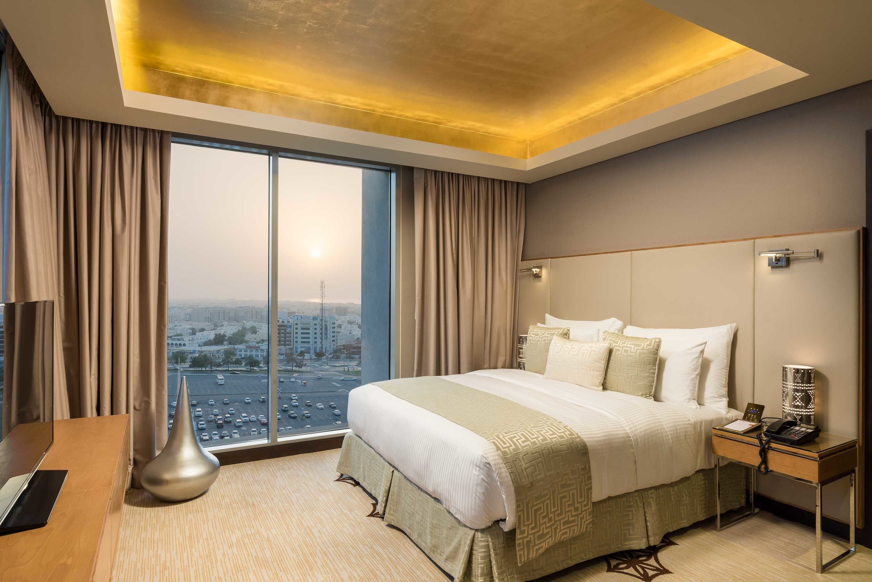 Habitación de hotel con una cama grande, un escritorio, una lámpara y vistas a la ciudad a través de la ventana.