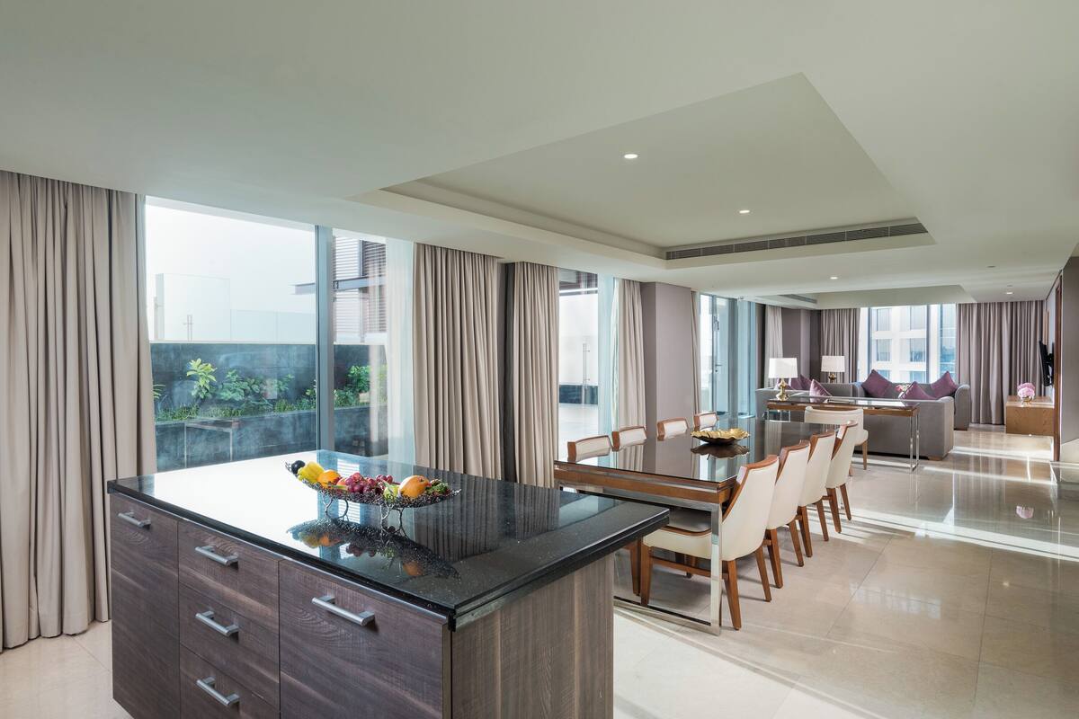 A modern kitchen with a central island, dining area with chairs, and a view of the outdoors.