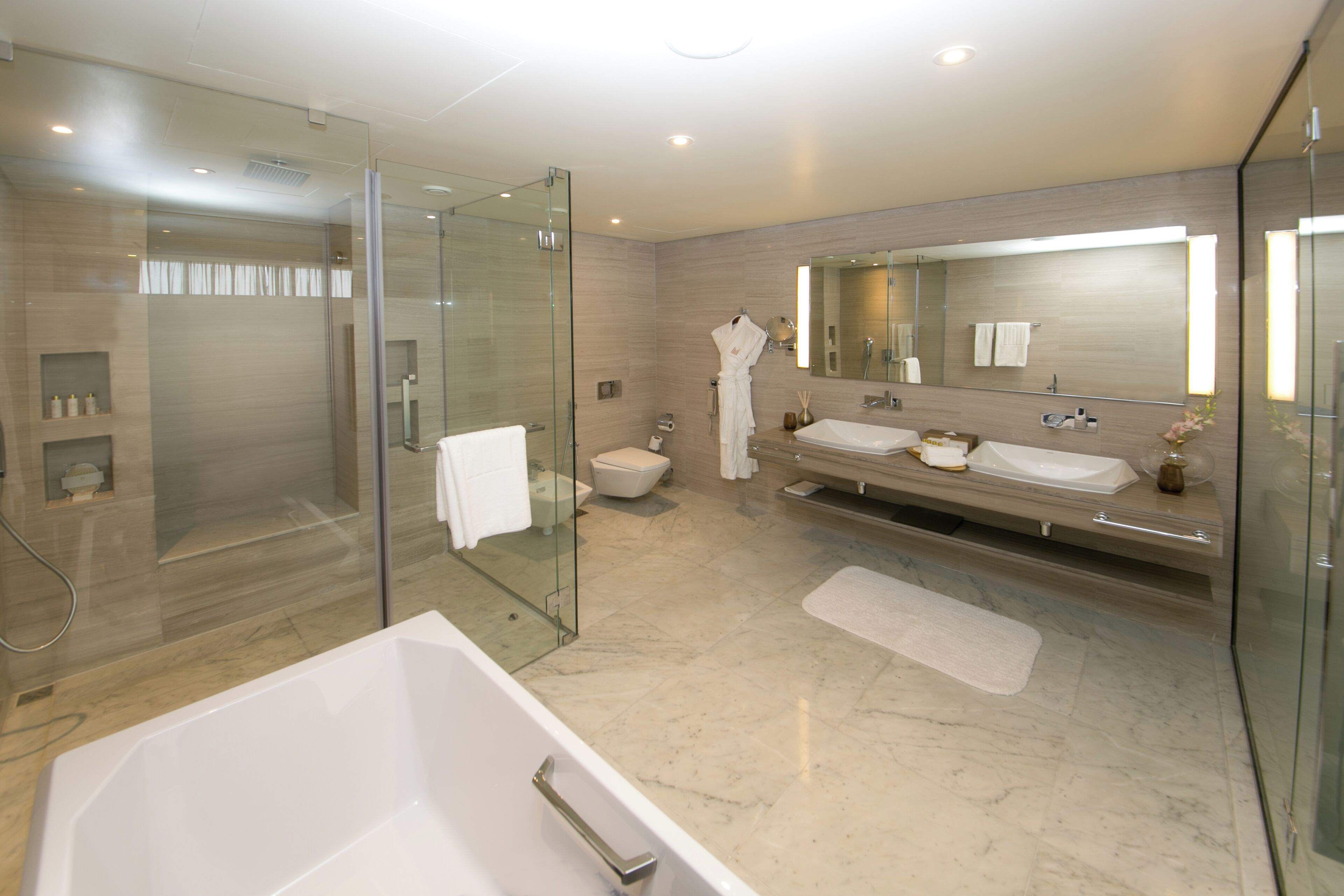 A modern bathroom with a glass-enclosed shower, a large bathtub, and a vanity with two sinks.