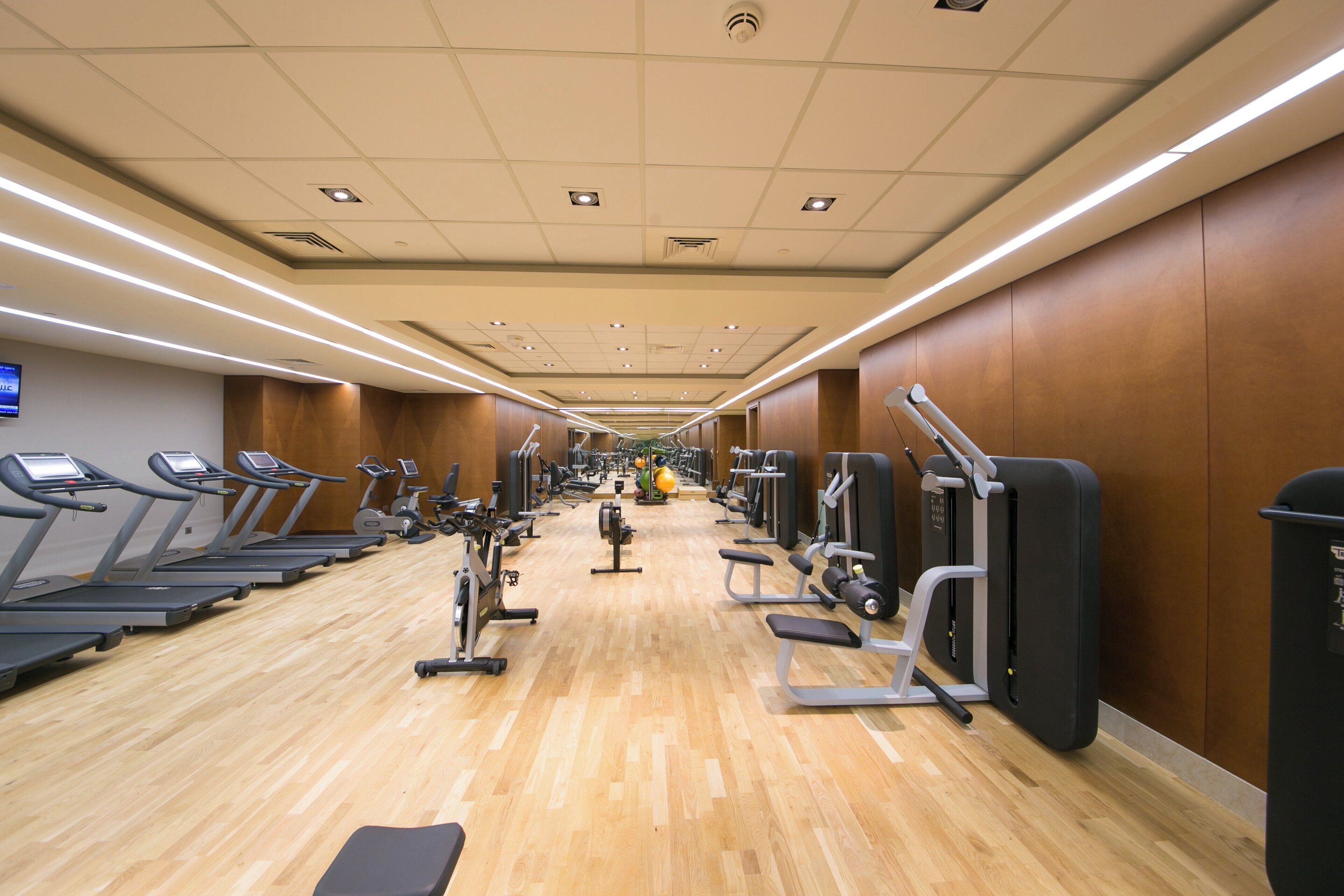 Un gimnasio con cintas de correr, elípticas y estaciones de pesas, distribuidas en un espacio amplio.