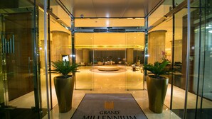 A modern hotel lobby with a glass entrance, a central seating area, and large potted plants. - Grand Millennium Muscat Apartments and Suites connected to Mall (Muscat)