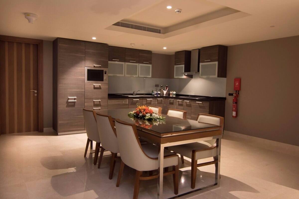 A modern kitchen with built-in appliances, a dining area with a glass table and chairs, and a fire extinguisher on the wall.