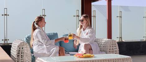 Two people sitting on wicker furniture outdoors with a glass table in front of them.