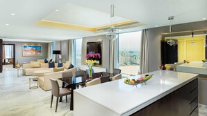 A modern hotel room with a large central island, a dining area, a sofa set, and a view of the city. - Grand Millennium Muscat Apartments and Suites connected to Mall (Muscat)