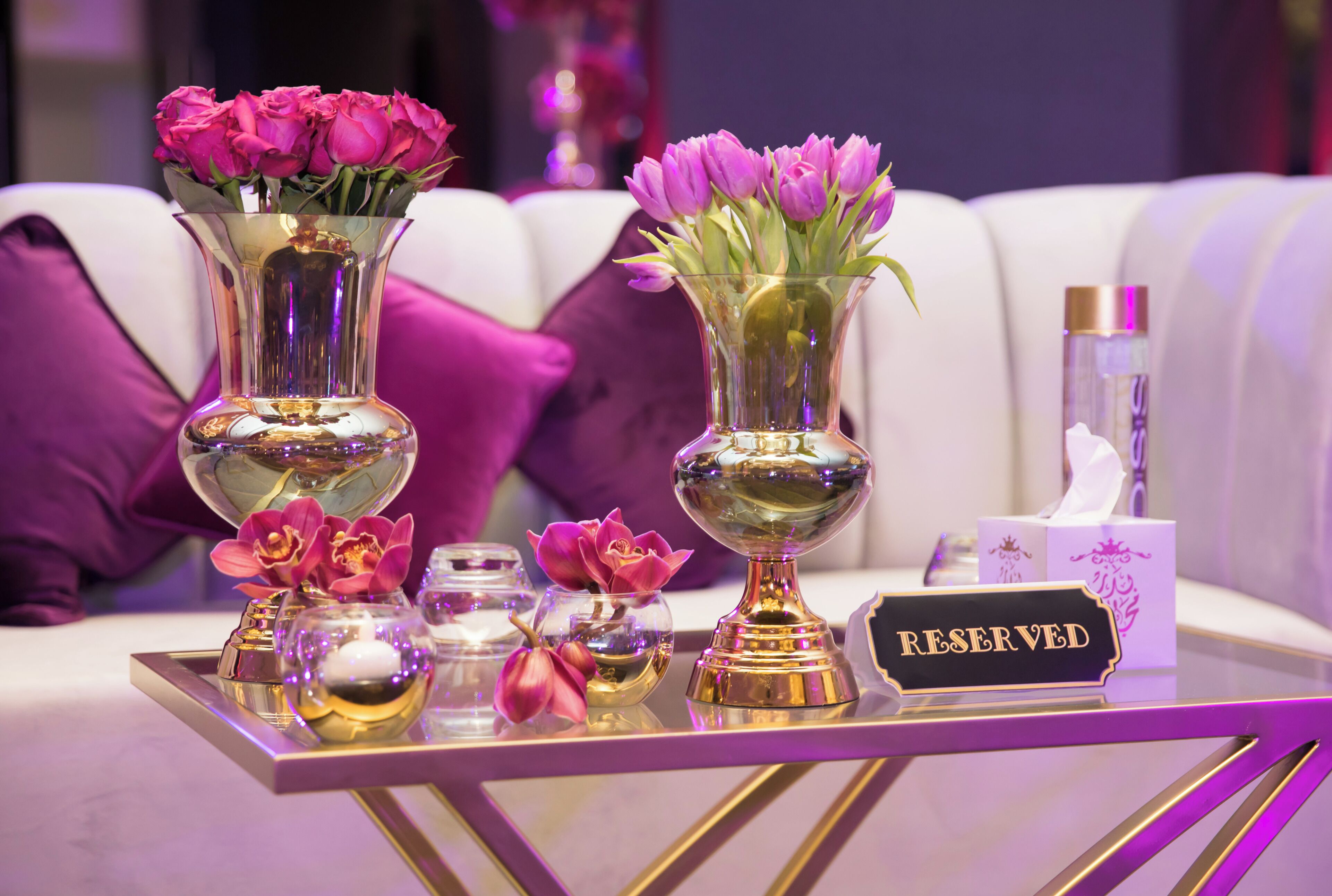 A table with two vases of pink flowers, a 'RESERVED' sign, and a tissue box.