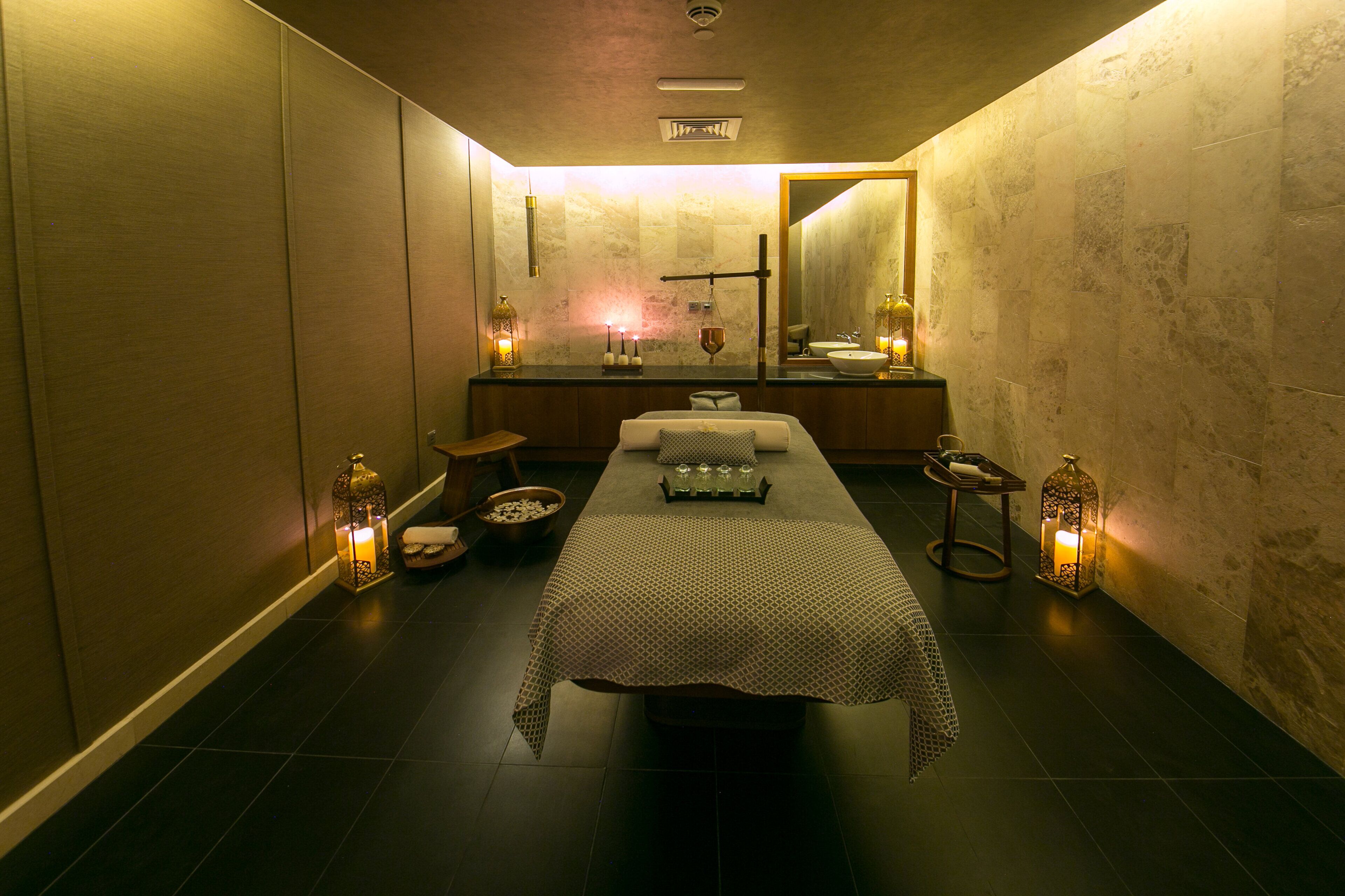Un cuarto de spa con una camilla de masaje, velas y un espejo.
