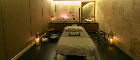 Un cuarto de spa con una camilla de masaje, velas y un espejo.