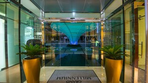 A modern hotel entrance with a glass facade, a central water feature, and a reception desk. - Grand Millennium Muscat Apartments and Suites connected to Mall (Muscat)
