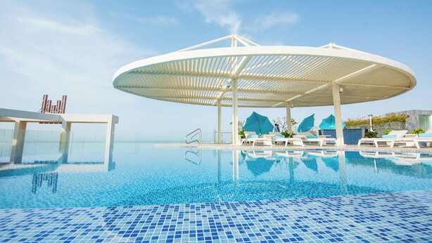 A swimming pool with a white canopy, lounge chairs, and a clear sky. - Grand Millennium Muscat Apartments and Suites connected to Mall (Muscat)