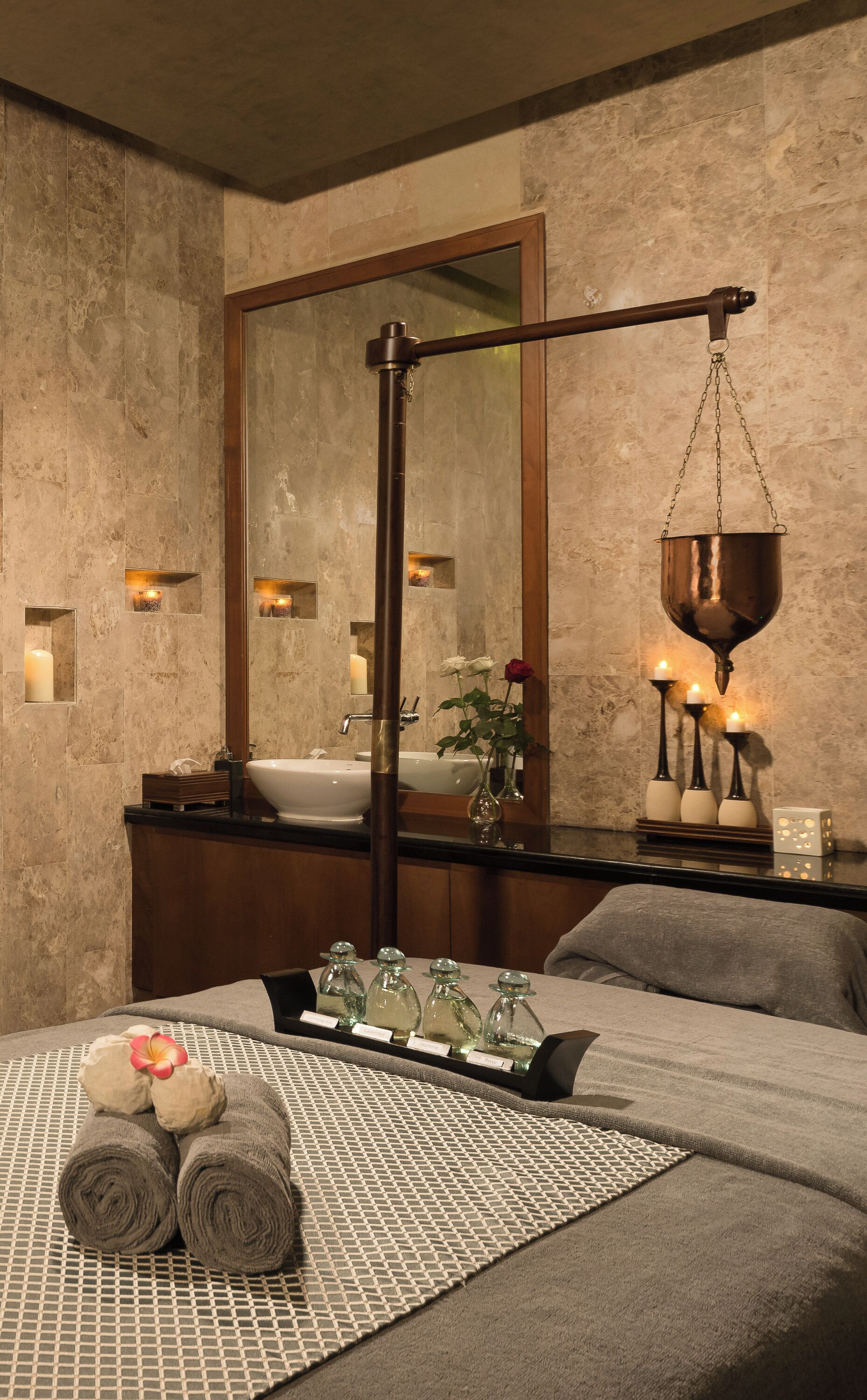 A spa room with a large mirror, a hanging copper pot, a bathtub, and a tray with towels and bottles.