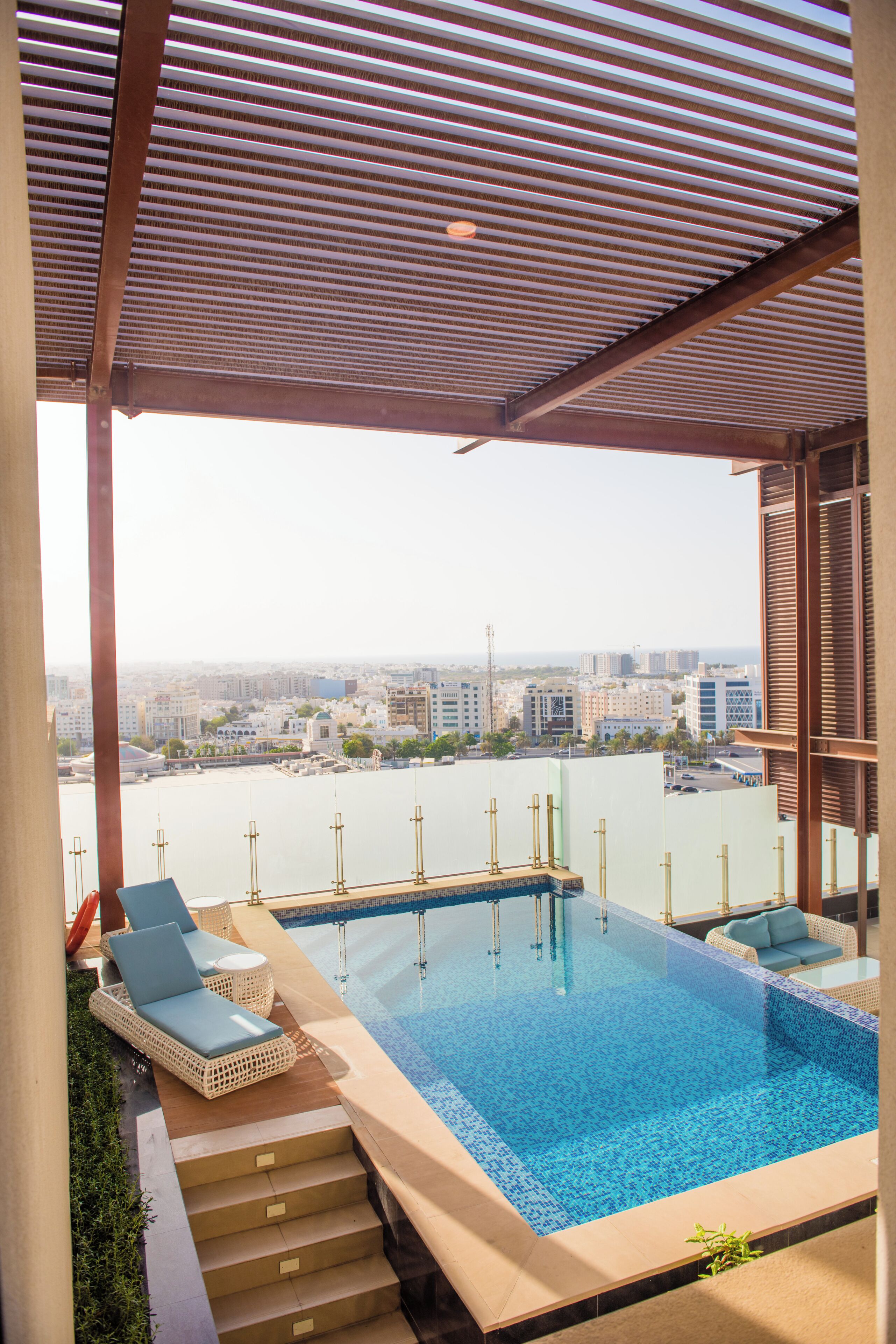 A rooftop infinity pool with lounge chairs, a view of the city, and a clear sky.