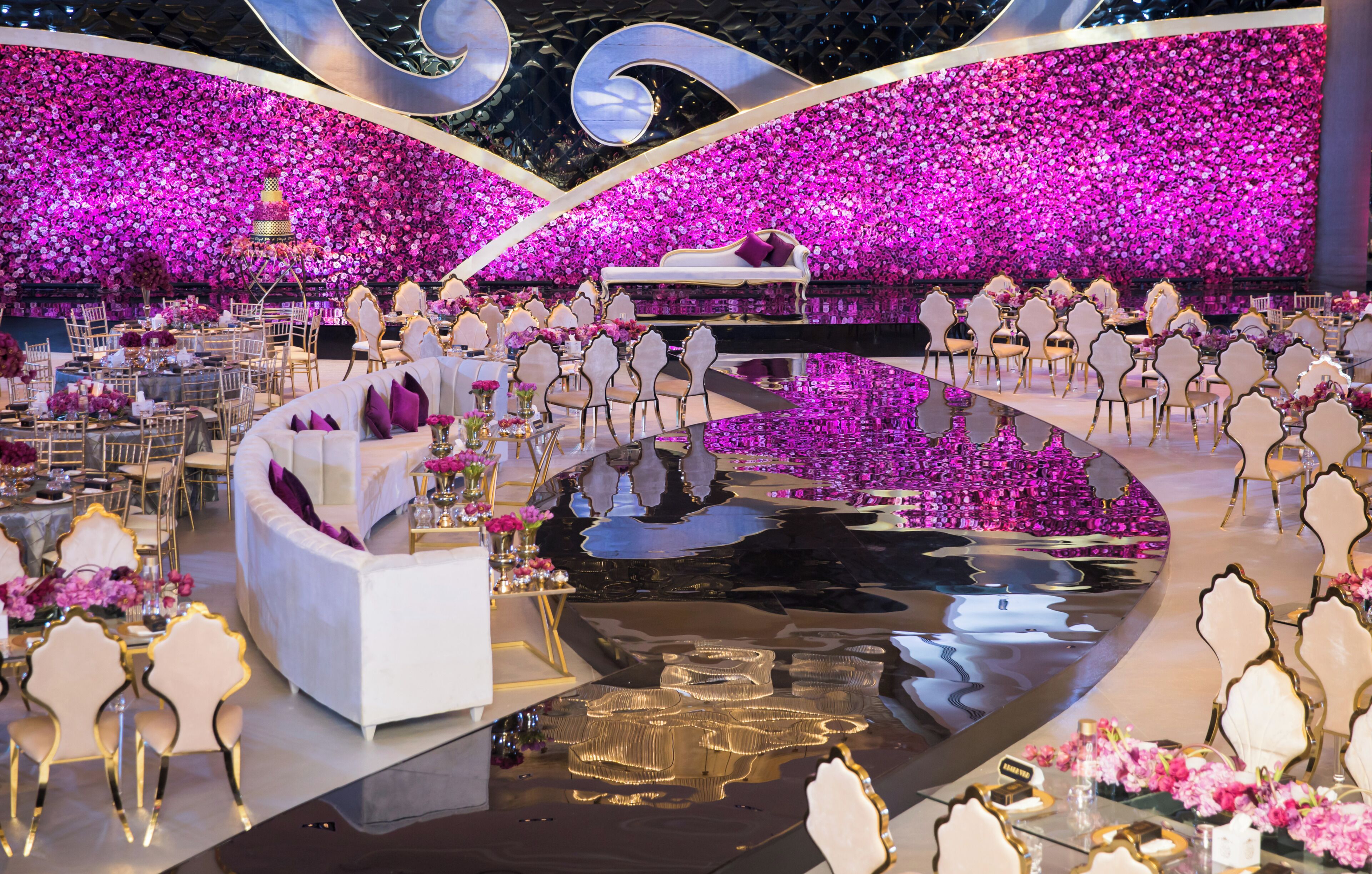 A formal event space with a reflective floor, white seating, and a floral backdrop.