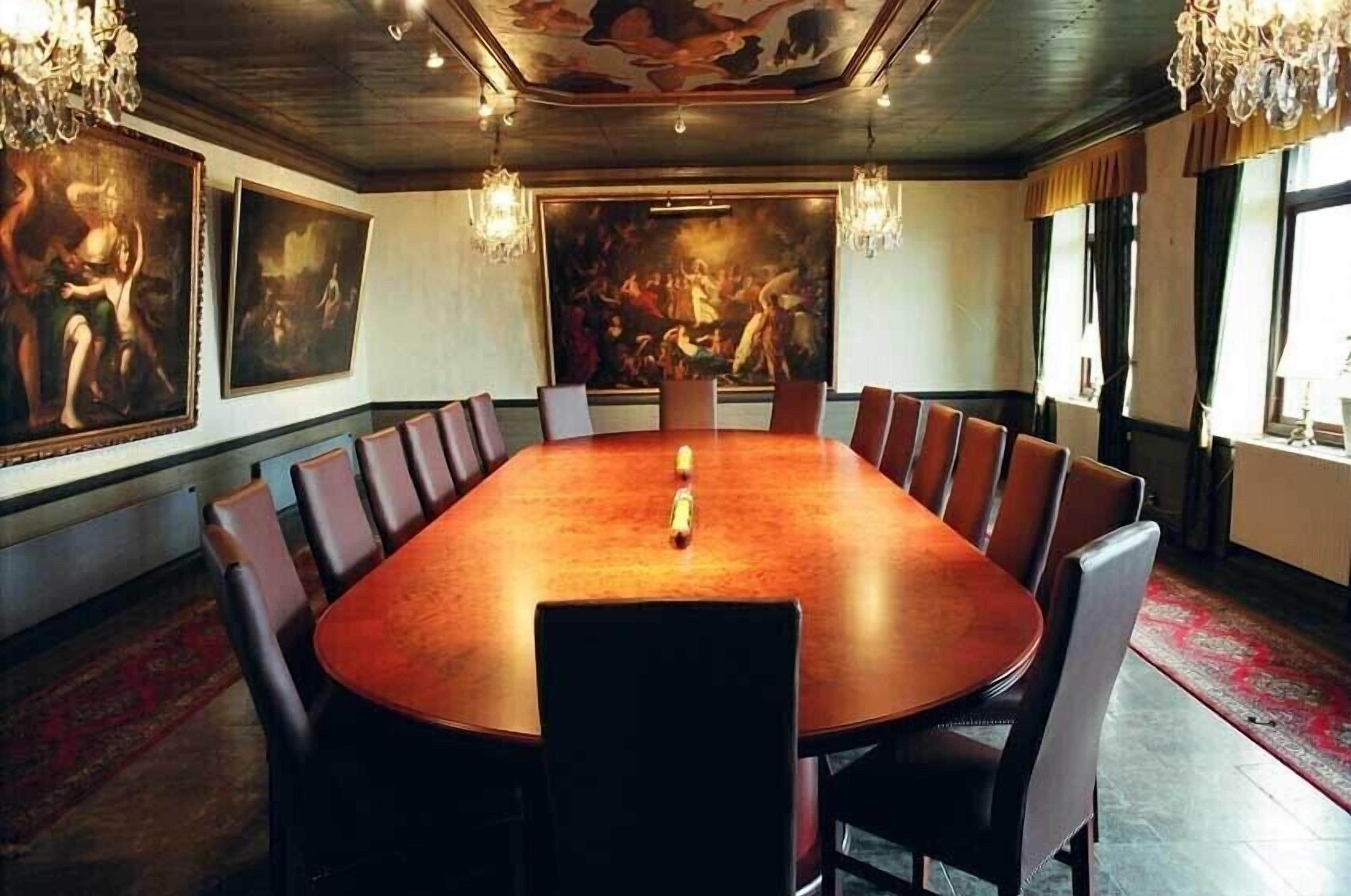 A conference room with a large round table, leather chairs, and artwork on the walls.
