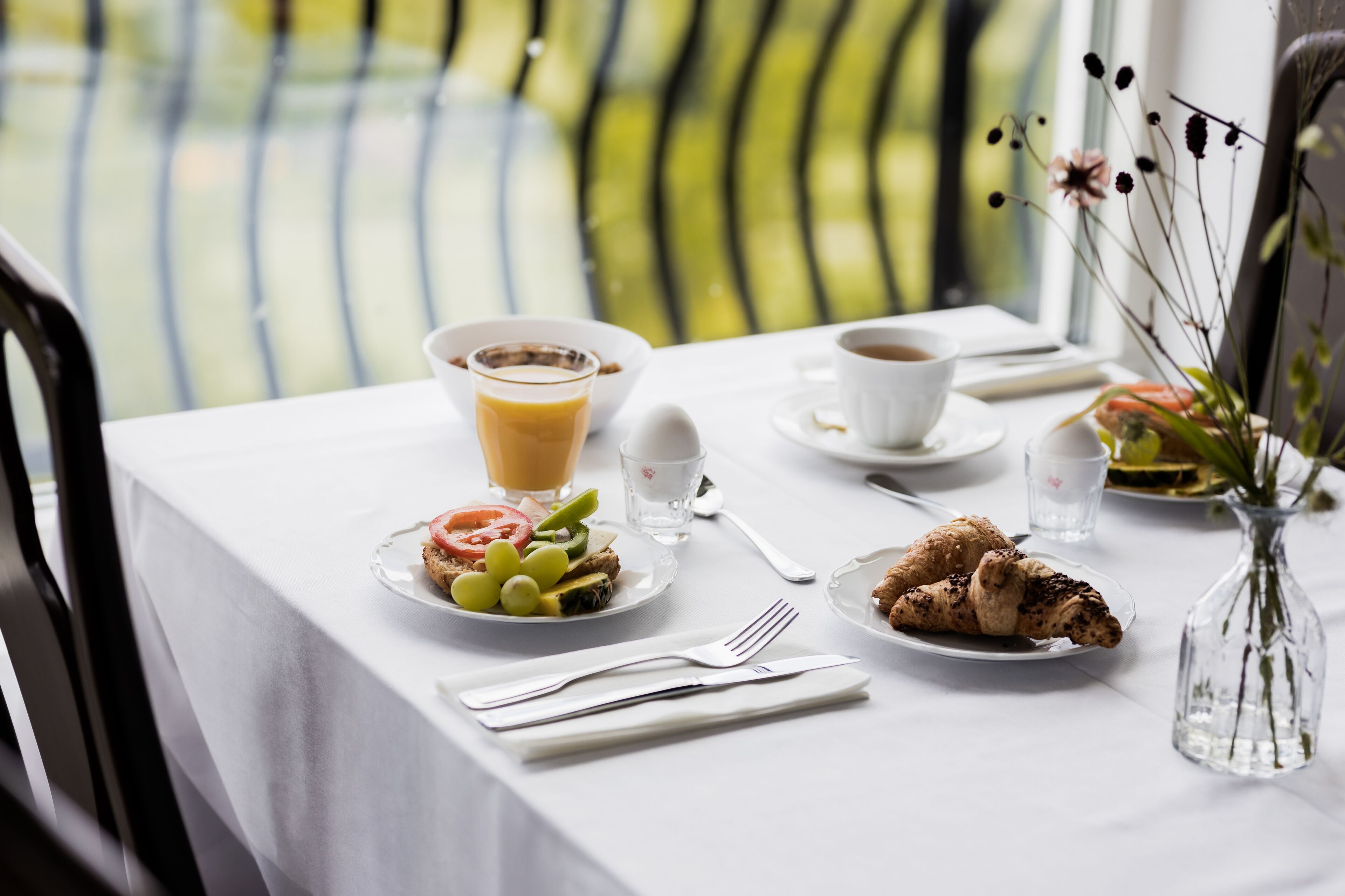 Un desayuno con una mesa dispuesta para dos, incluyendo platos con comida, una taza de café y un vaso de zumo de naranja.