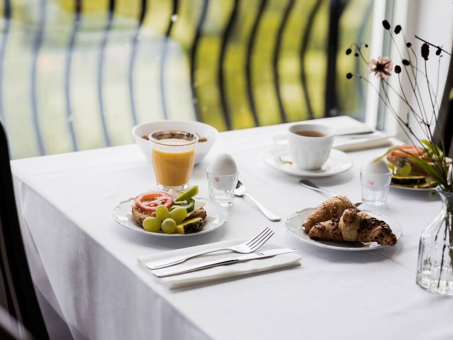 Un desayuno con una mesa dispuesta para dos, incluyendo platos con comida, una taza de café y un vaso de zumo de naranja.