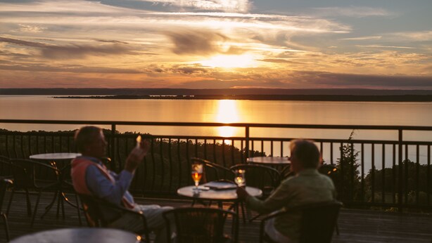A sunset view from an outdoor dining area with tables and chairs, overlooking a body of water. - Hotel Gyllene Uttern (Gränna)