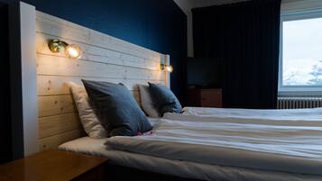Habitació d'hotel amb un capçal de llit de fusta, un llit amb roba de llit blanca, dos nus i una taula de nit, i una televisió.