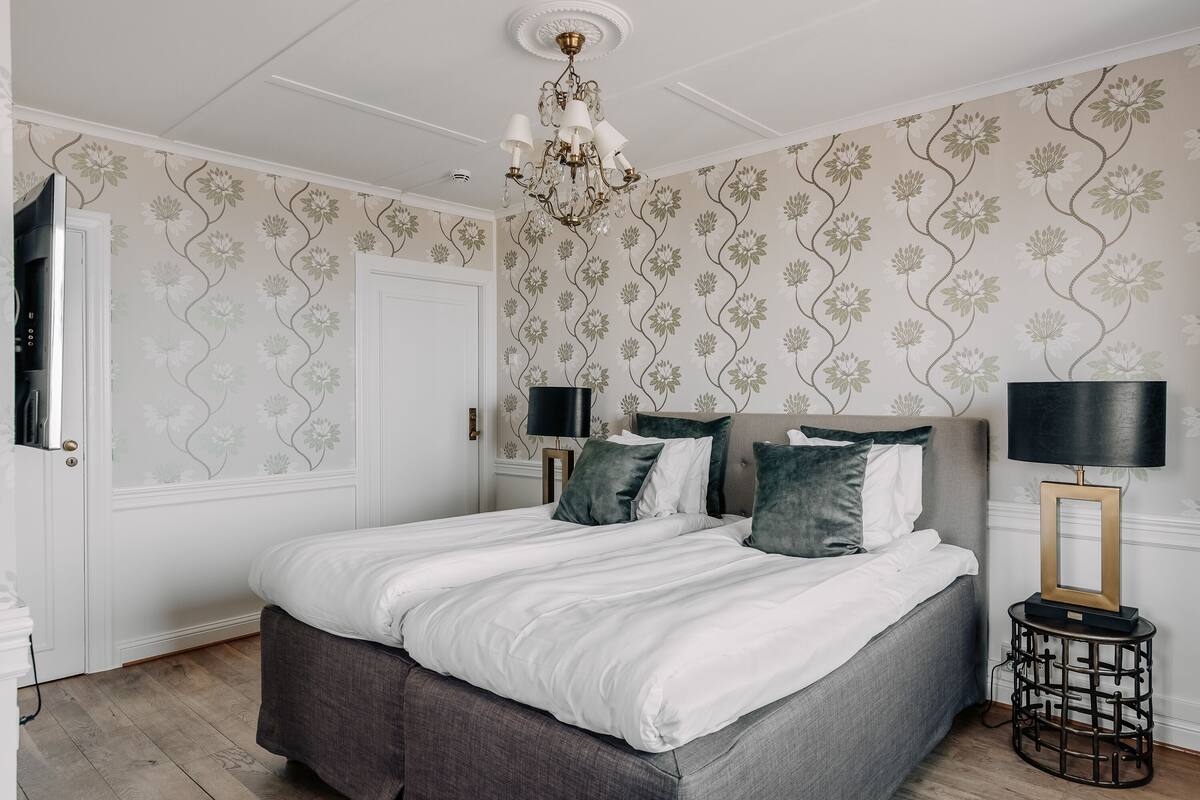 A bedroom with a large bed, a chandelier, and floral wallpaper.