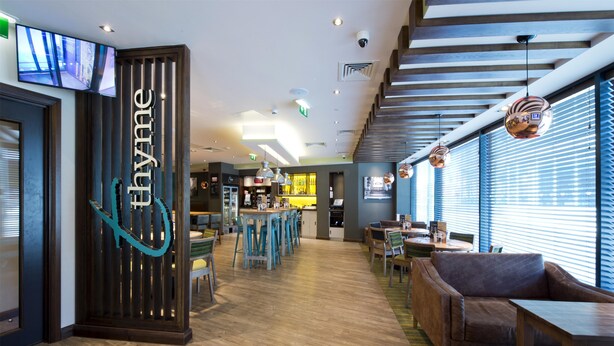 Een moderne hotellobby met een bar, zitplaatsen en een groot scherm waarop een straatbeeld te zien is.
