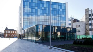 Een modern gebouw met grote glasramen, een verharde looppad en een lantaarnpaal.