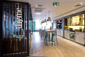 A modern restaurant interior with a bar area, wooden flooring, and pendant lighting. - Premier Inn Buxton (Buxton)