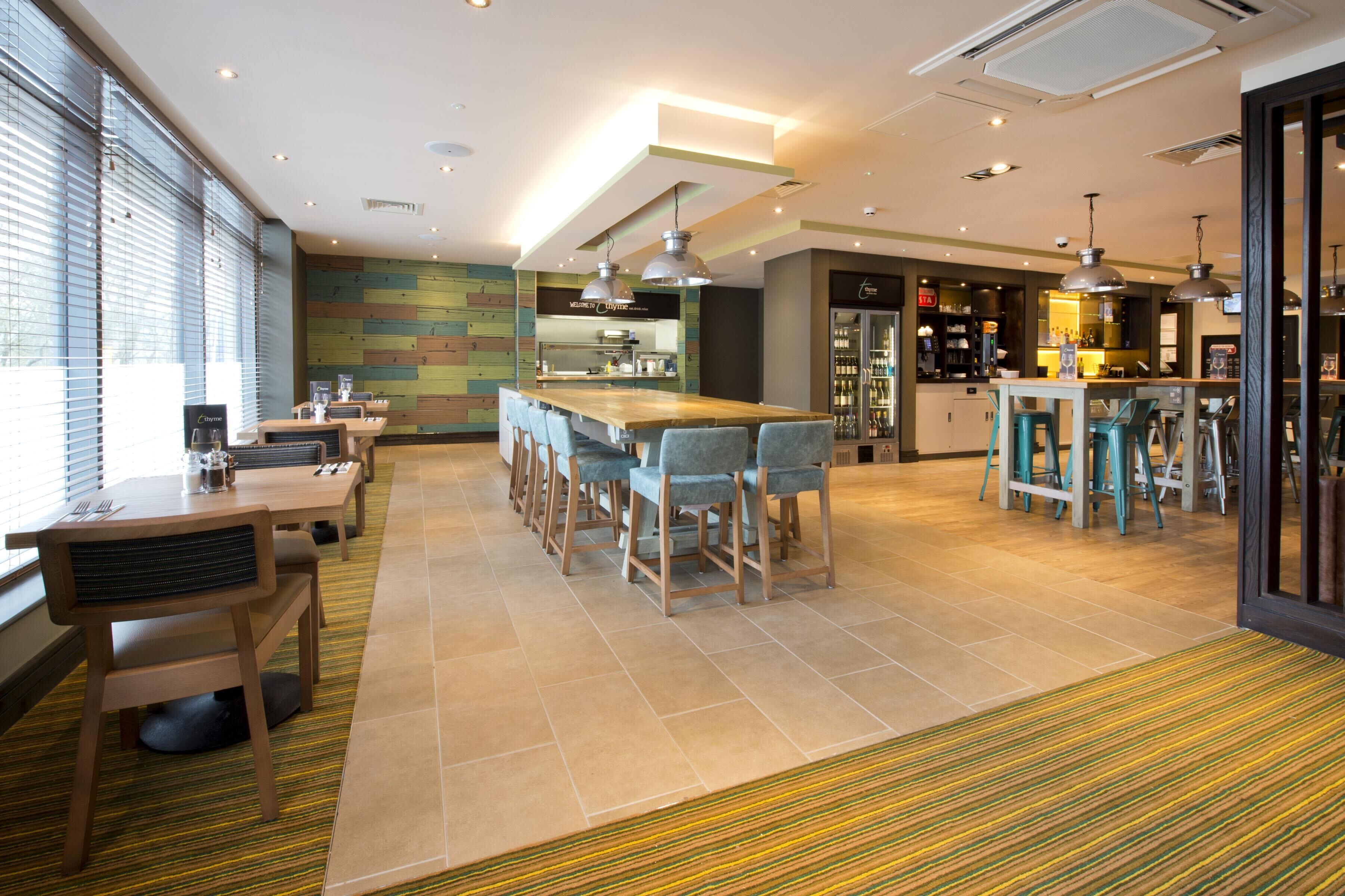 A modern hotel lobby with a bar area, seating arrangements, and a kitchen in the background.