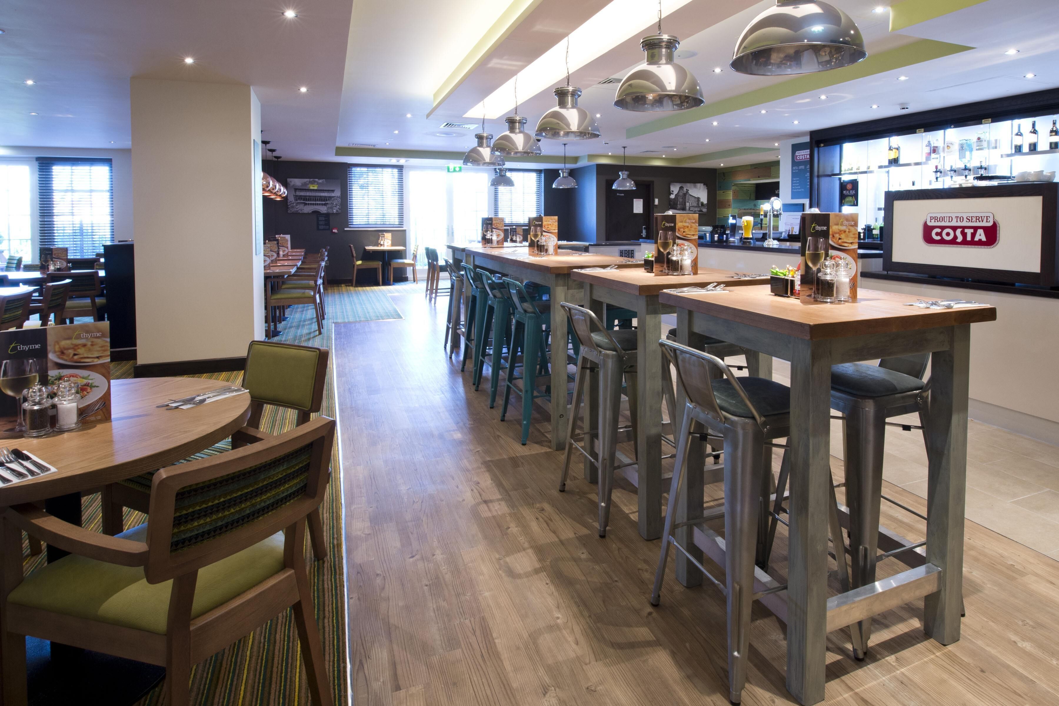 A modern restaurant with bar stools, high tables, and pendant lighting.