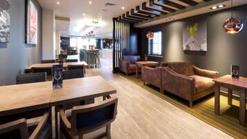 Un restaurante con mesas y sillas de madera, una zona de bar y una estatua en la pared.