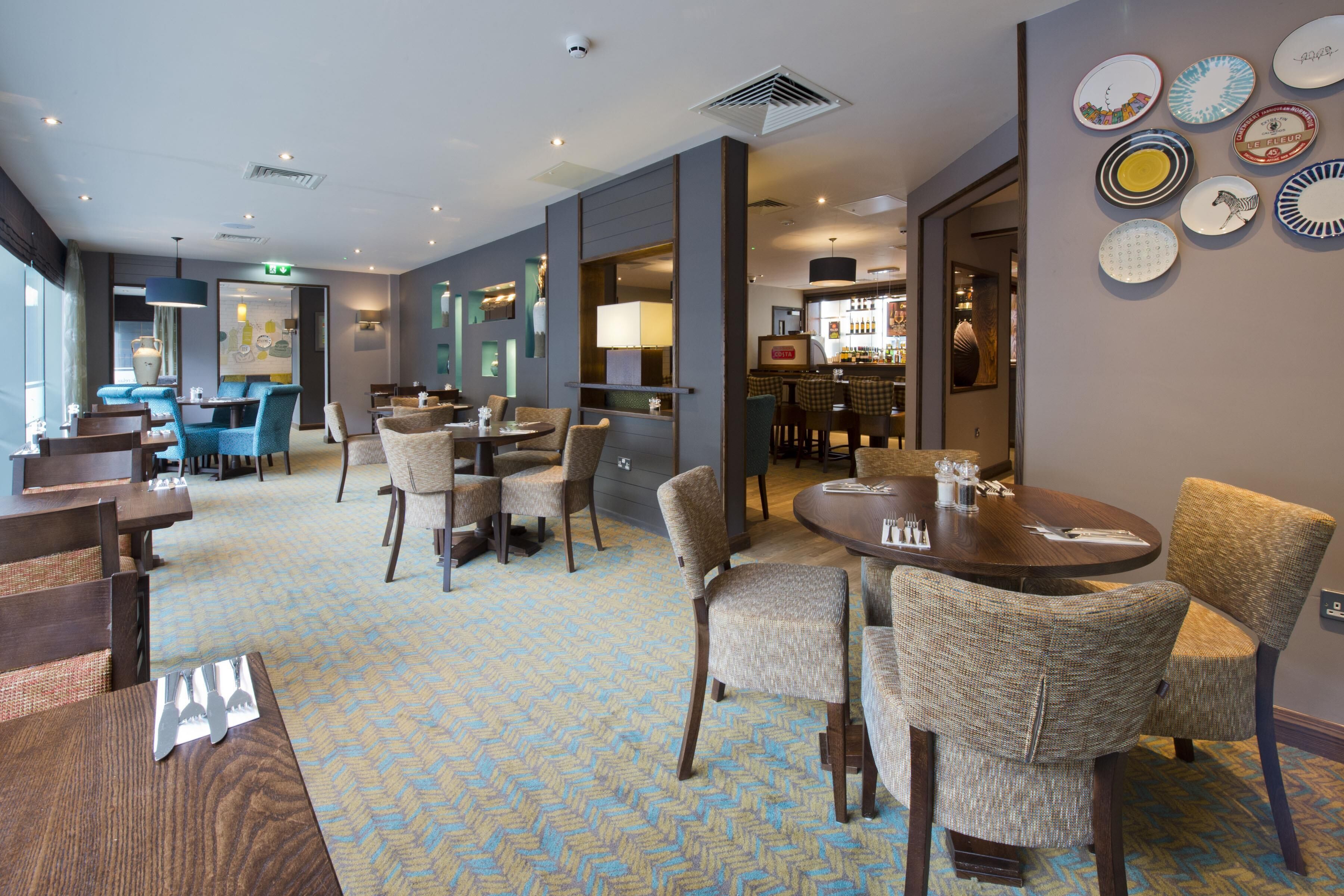 Un hall d’hôtel comprenant un bar, des espaces aménagés avec des sièges et un tapis à motifs.