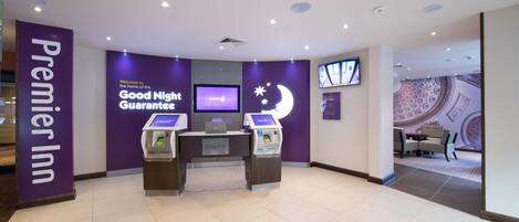 Egy bejelentkező részleg, amelyen egy „Premier Inn” felirat, egy monitor és egy „Nyugodt éjszakát garantáljuk” felirat található.