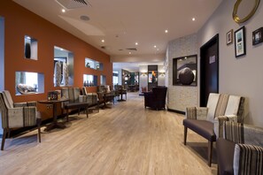 Un hall d’hôtel doté d’un plancher en bois, d’un espace salon avec des chaises et des tables, et d’un comptoir de réception.