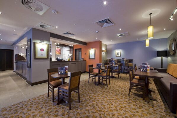 A restaurant with tables and chairs, a bar area, and a patterned carpet. - Premier Inn Exeter City Centre (Exeter)