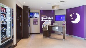 A hotel lobby with a vending machine, a reception desk, a television, and a wall with a moon and stars design. - Premier Inn Honiton (Honiton)