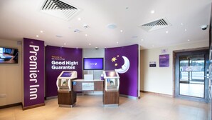 Ein Empfangsbereich eines Premier Inn mit einer Rezeption, einem Fernsehbildschirm und einem digitalen Kiosk.