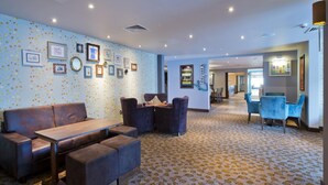 A hotel lobby with a patterned carpet, a seating area with a sofa and chairs, and a wall decorated with framed pictures. - Premier Inn London Archway (London)