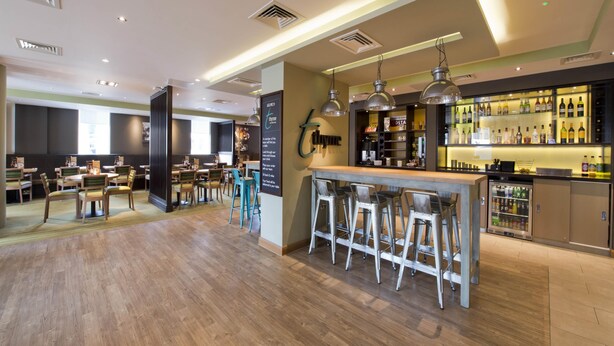A modern bar area with stools, a bar counter, and a variety of bottles. - Premier Inn London Sidcup (Sidcup)