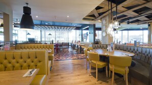 Een restaurant met houten vloeren, gele zitbankjes en een combinatie van tafels en zitbanken.