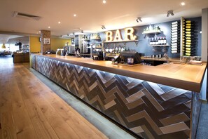 A bar area with a herringbone floor pattern, a counter with a cash register, and shelves with bottles and glasses. - Premier Inn London Uxbridge (Uxbridge)