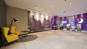 A hotel lobby with a reception desk, a seating area with yellow chairs, a large cityscape mural, and a clock. - Premier Inn Newcastle City Centre The Gate (Newcastle-upon-Tyne)