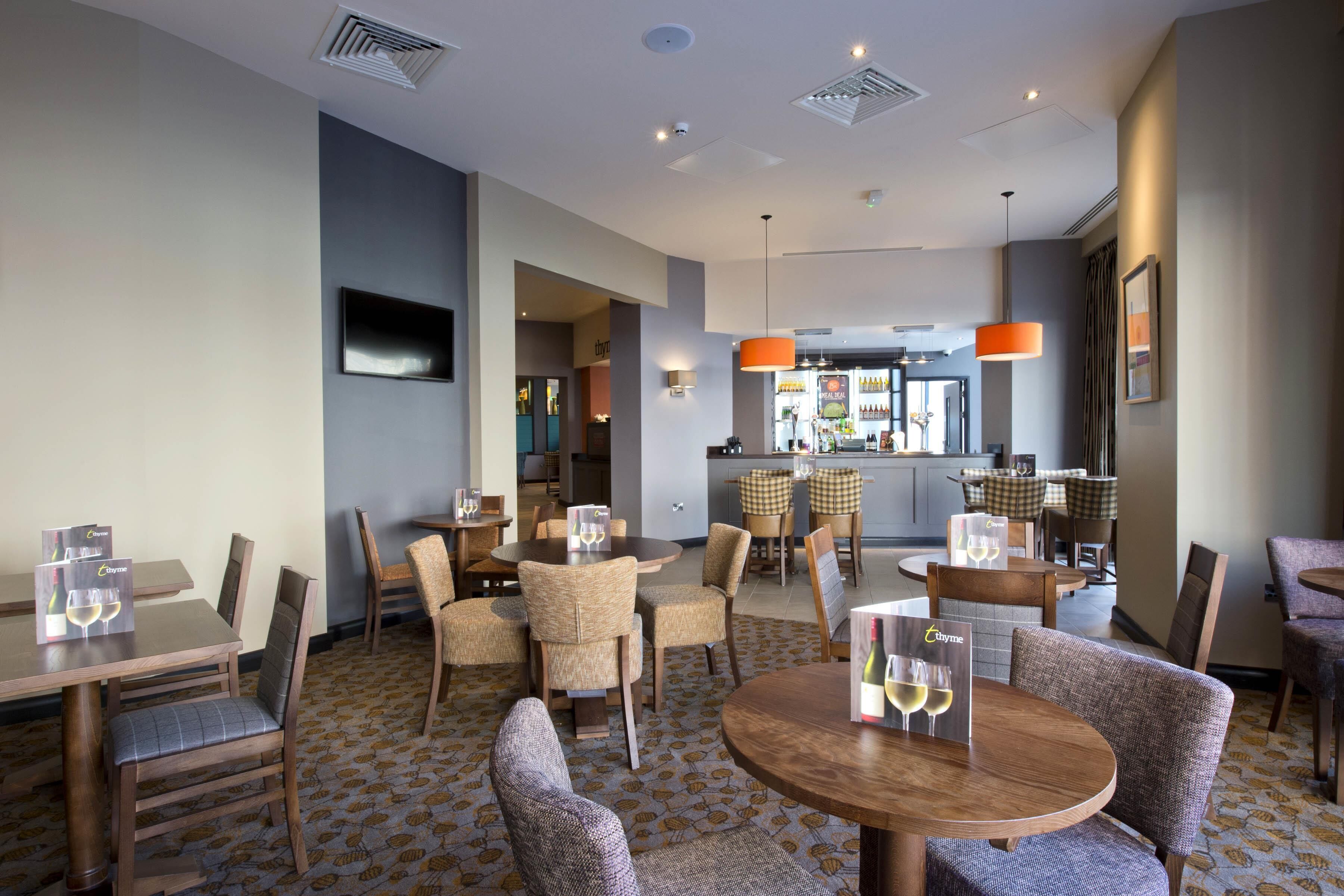 Un comedor de hotel con varias mesas y sillas, un bar y un televisor montado en la pared.