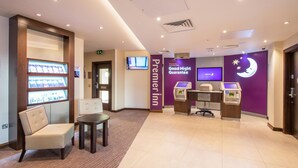 Et hotel lobby med reception, digital skærm, siddeområde og et 'Premier Inn' skilt.