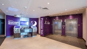 Eine Hotte lobby mit einer Rezeption, einer digitalen Anzeige, einer Überwachungskamera und zwei Aufzügen.