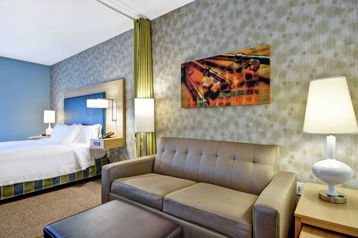 Een hotelkamer met een bed, een bank, een bureau met een lamp en een schilderij aan de muur.