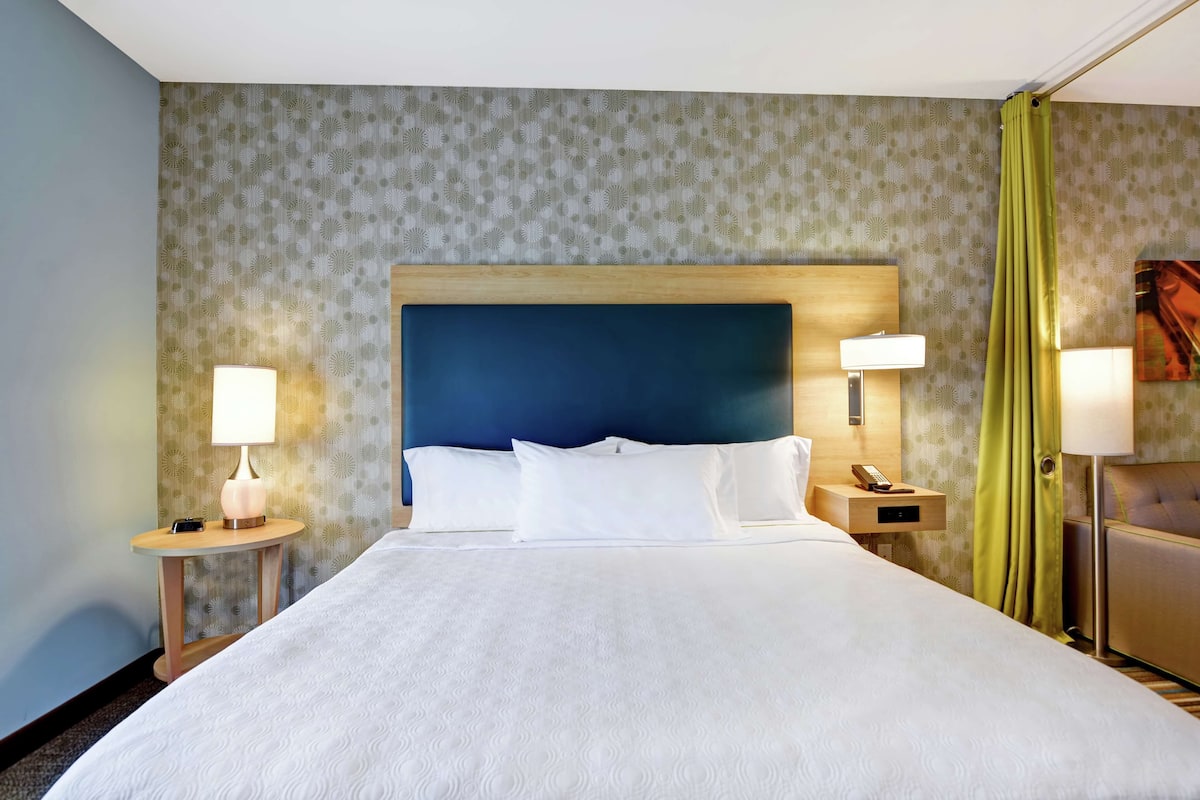 Een hotelkamer met een groot bed, twee nachtkastjes met lampen, een hoofdeinde en een gordijn.