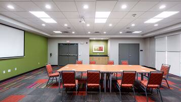 A conference room with a long table, multiple chairs, a projector screen, and a carpeted floor.