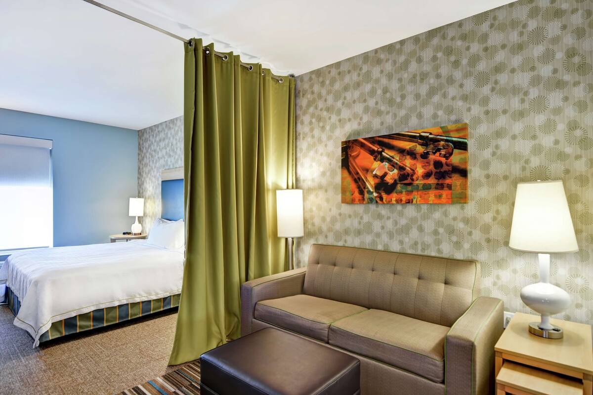 Een hotelkamer met een bed, een bank, een poef en een schilderij aan de muur.